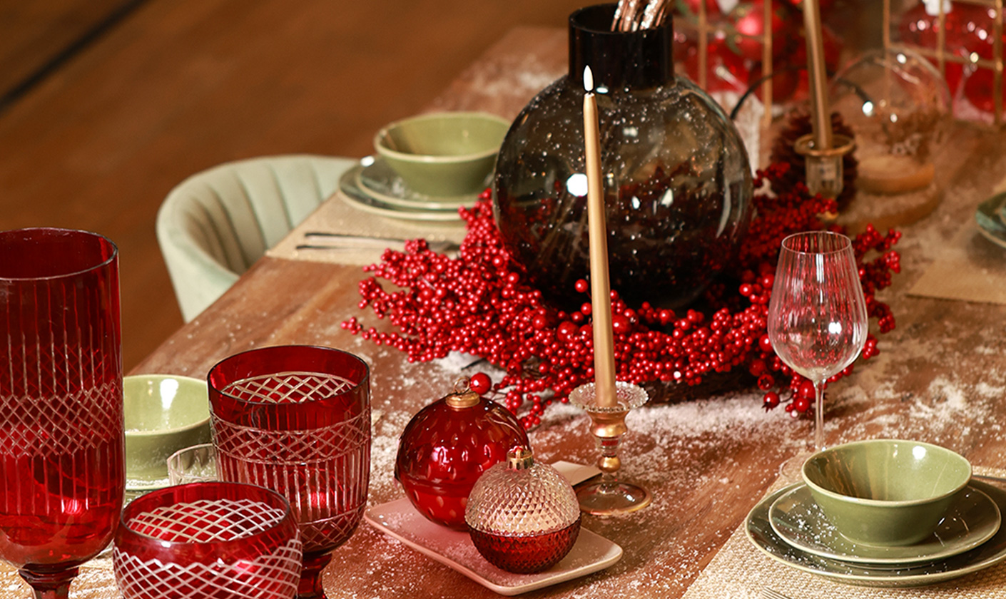 Festive dining table with red glassware, candles, and holiday tableware.